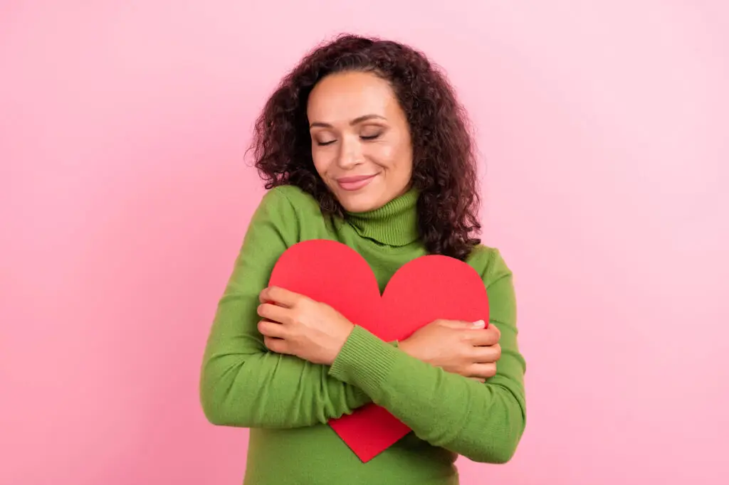 Young woman smiling with closed eyes while hugging a heart pillow.