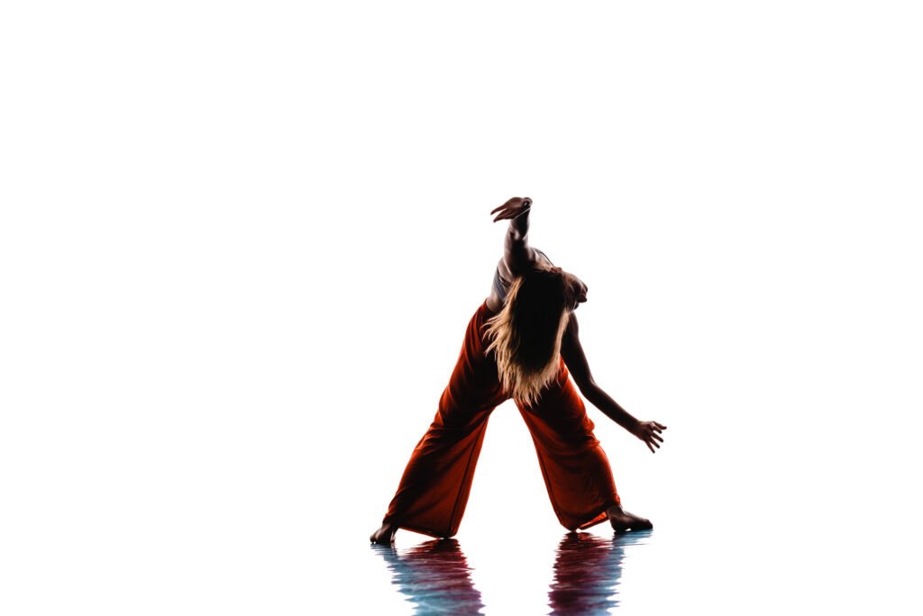 Woman doing somatic dance, leaning forward, arms outstretched, silhouette