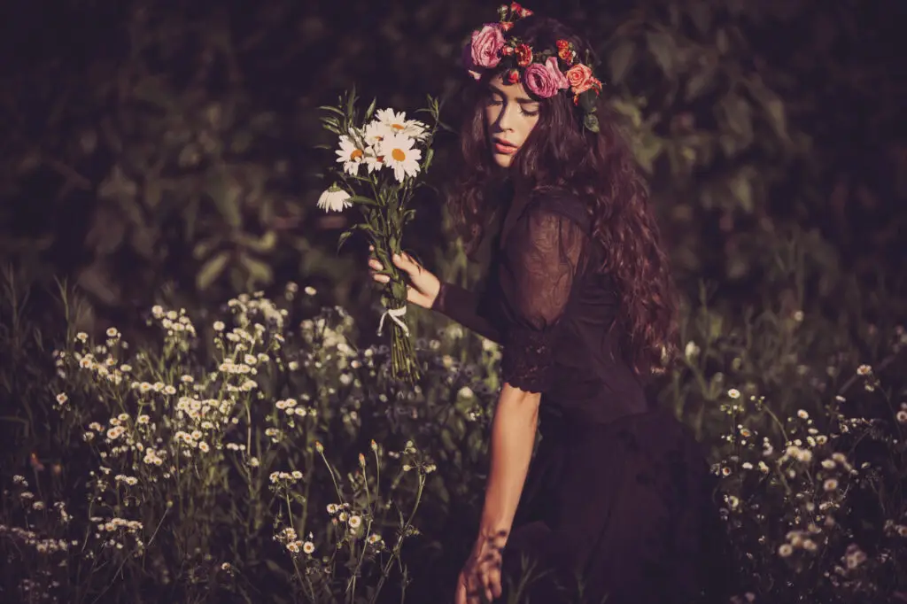 Young woman with flower crown holding bouquet of daises in a field of wild flowers