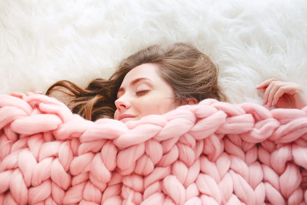 Young woman sleeping in cozy pink knit blanket.