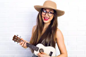 Young woman wearing rimmed hat playing white ukulele