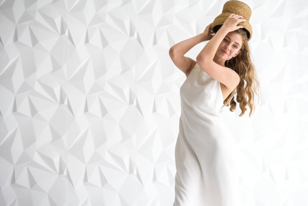 Young woman in white dress on white background playfully tipping hat