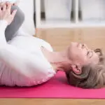 Woman on bright pink yoga may, lying on back, stretching legs