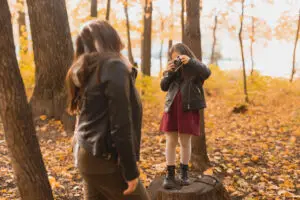 Young girl taking her mother's picture with a vintage camera in a park during autumn.