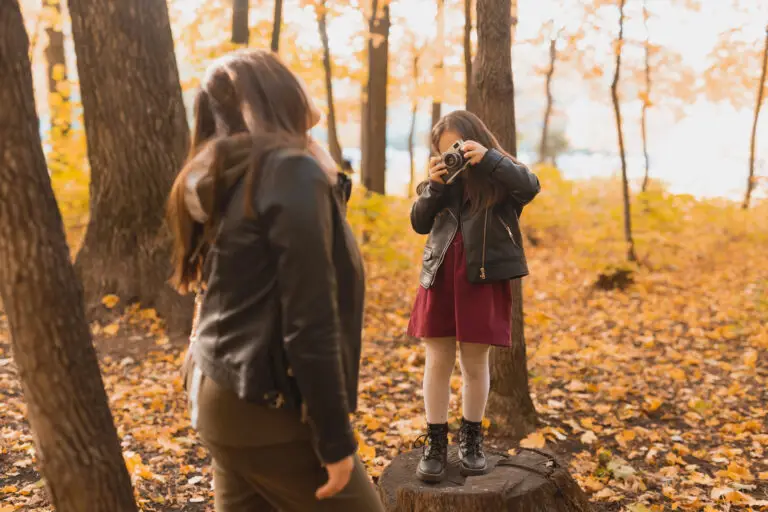 Young girl taking her mother's picture with a vintage camera in a park during autumn.