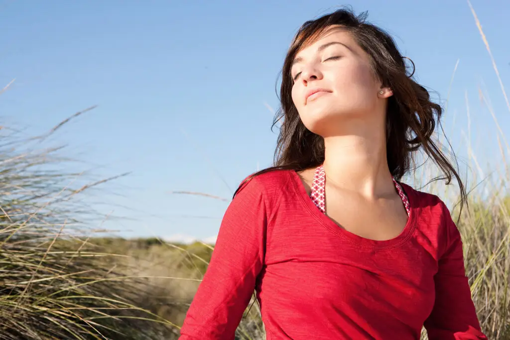 Woman outdoors with eyes closed experiencing sunlight and fresh air, illustrating how sensory experiences influence stress and relaxation.