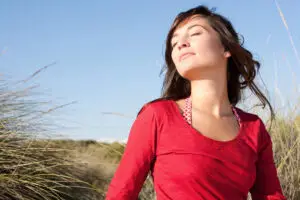 Woman outdoors with eyes closed experiencing sunlight and fresh air, illustrating how sensory experiences influence stress and relaxation.
