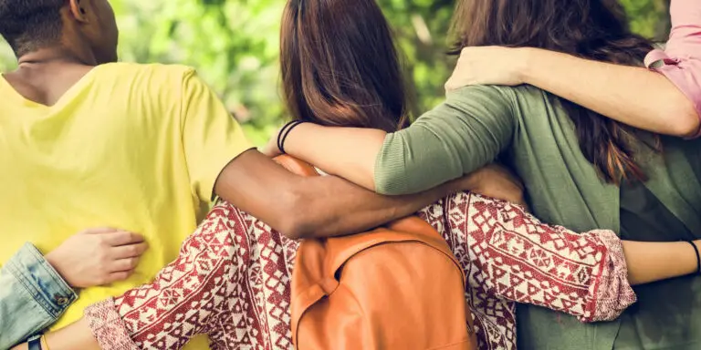 A group of people sitting outdoors with their arms around one another, representing human connection and the relationships that shape our lives.