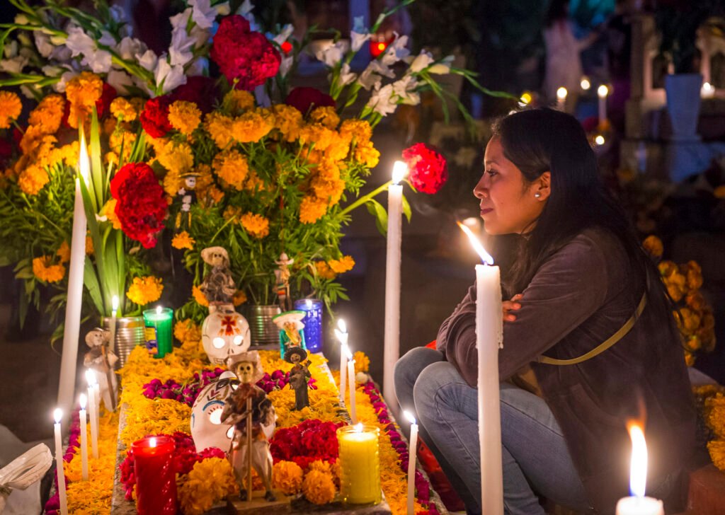 Woman honoring loved ones beside a flower-filled Día de los Muertos ofrenda in Oaxaca, Mexico.