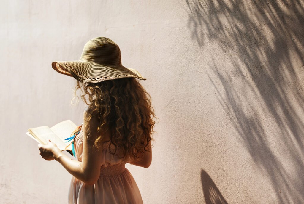 Woman in a straw hat reading beside palm shadows